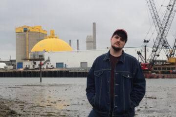 Connor Gilroy of the band Gilroy standing infront of an industrial harbor scape